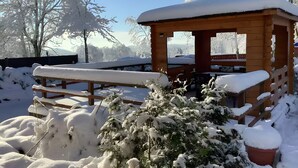 A wooden cabin with a bench and snow-covered plants in a snowy outdoor setting.