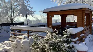 A wooden cabin with a bench and snow-covered plants in a snowy outdoor setting.