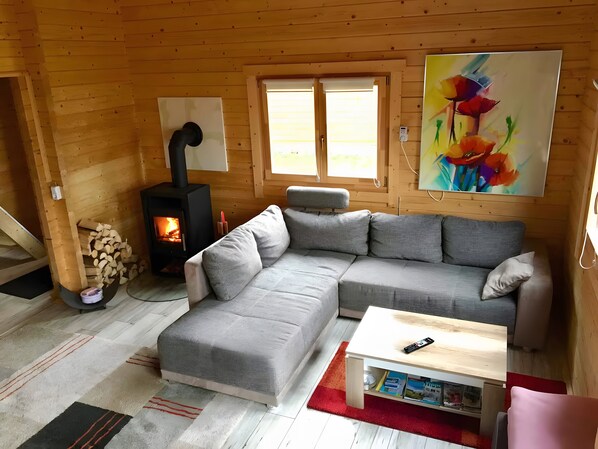 A cozy cabin interior with a sectional sofa, a small table, a fireplace, and a painting on the wall. - Ferienhaus 'Summit Butze Hohegeiß Blockhütte' mit WLAN und Klimaanlage (Braunlage)