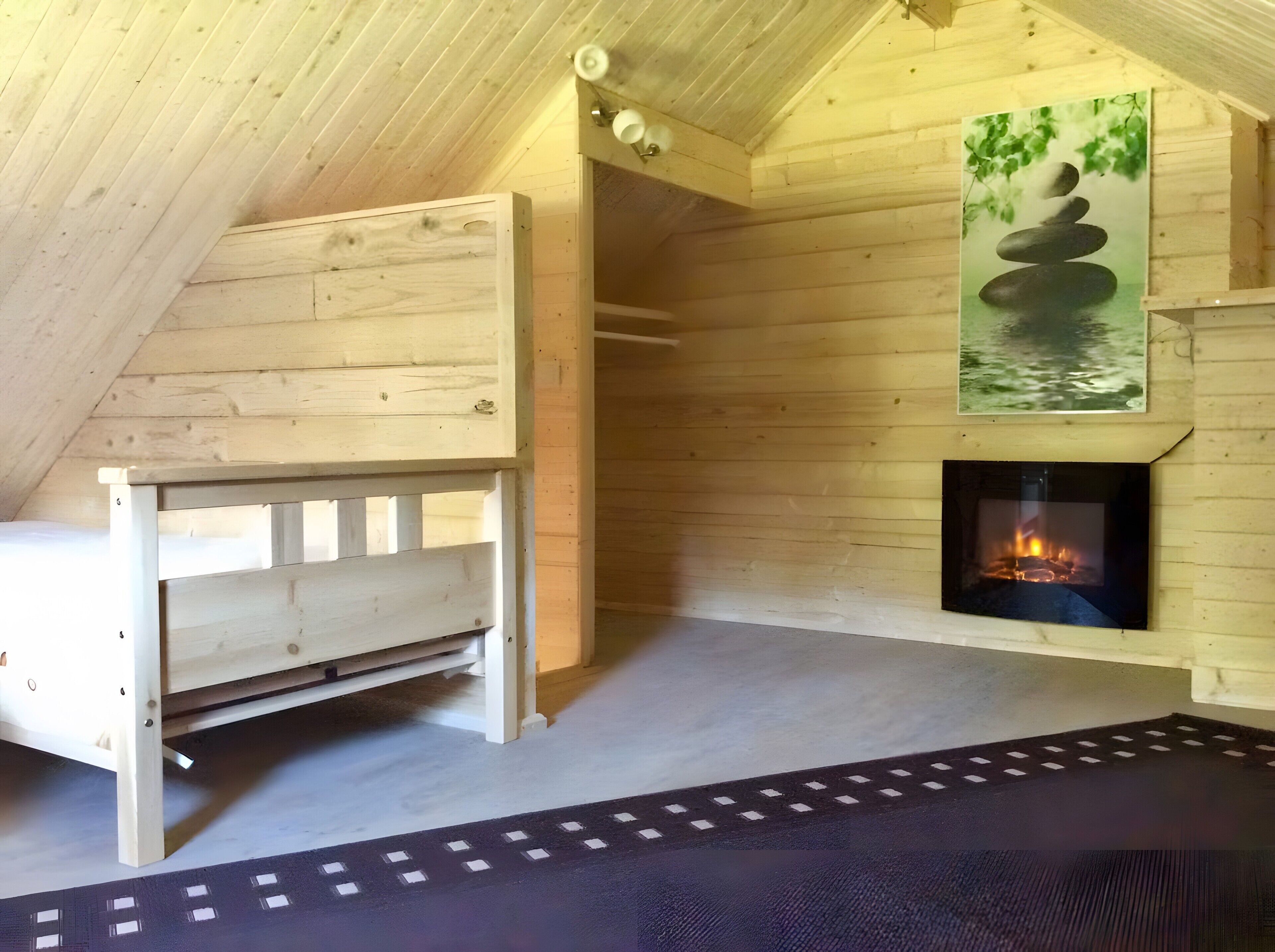 A wooden interior with a bed, a fireplace, and a painting of a rock stack.