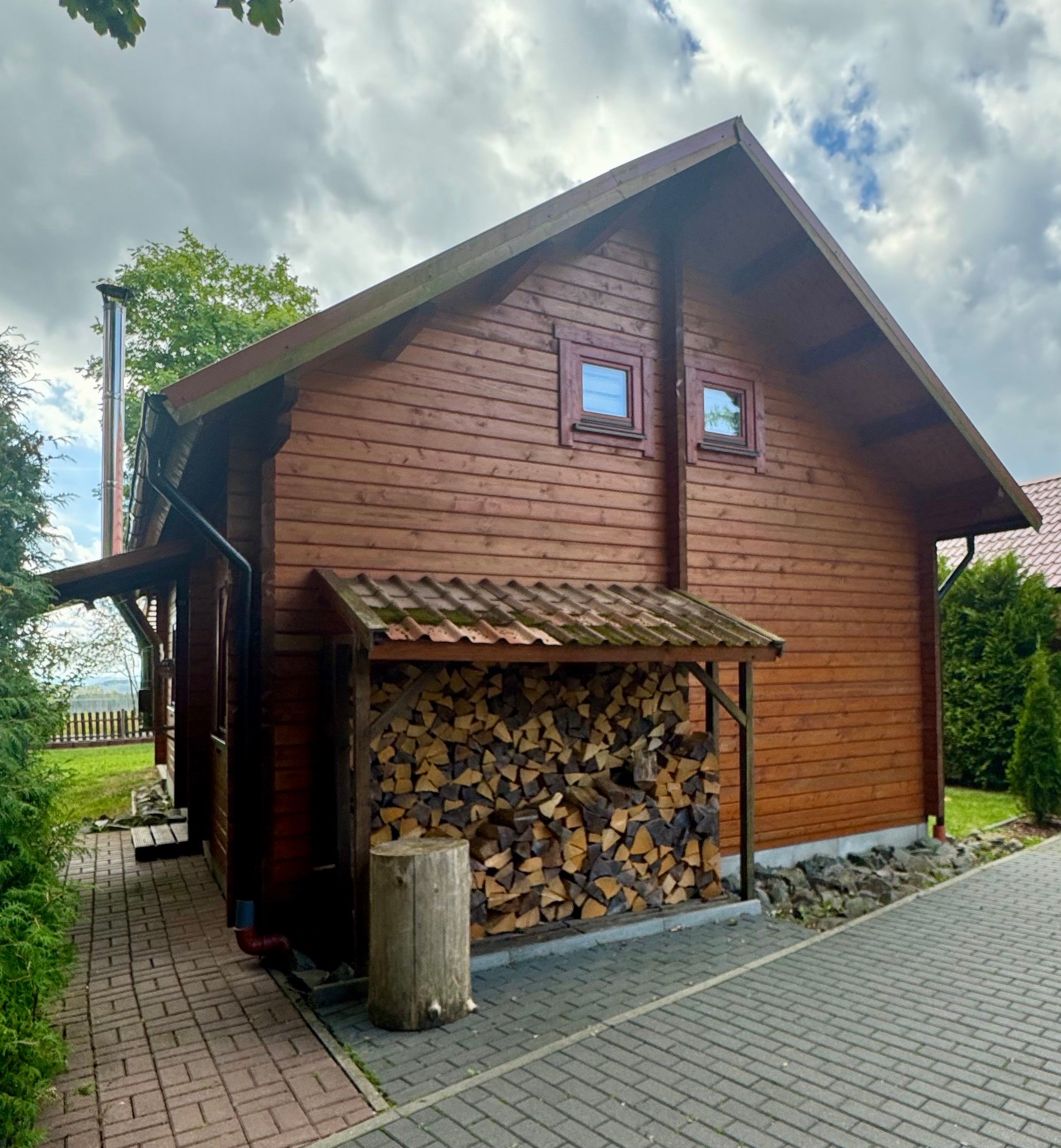Une cabane en bois dotée d’un porche abrité, d’une pile de bois de chauffage et offrant une vue sur le paysage environnant.