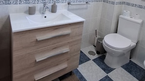A bathroom with a white sink, wooden vanity, a mirror above the sink, a toilet, and patterned floor tiles.