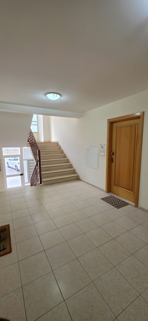 A spacious hallway with a tiled floor, a wooden door, and a staircase leading to another level.