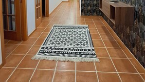 A hallway with tiled flooring, wooden doors, a patterned rug, recessed ceiling lights, and a decorative wall with a mirror.