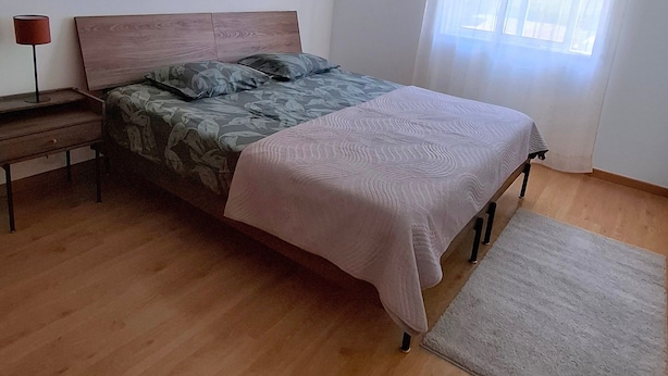 A bedroom with a bed, bedside table, lamp, and a window with curtains.