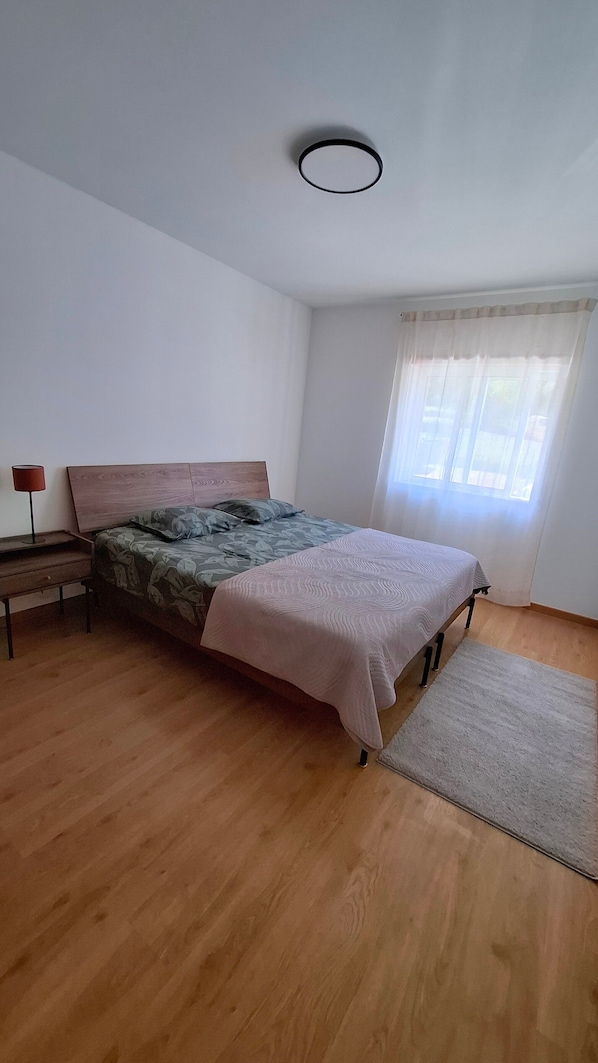 A bedroom with a bed, bedside table, lamp, and a window with curtains.