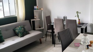 Uma sala de estar moderna com um sofá, mesa de jantar, cadeiras e uma pequena planta.