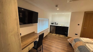 Une chambre de taille modeste comprenant un lit, un bureau, une chaise, un téléviseur, un four à micro-ondes et une petite kitchenette.