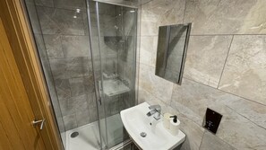 Une salle de bain moderne avec une douche en verre, un lavabo blanc et un mur recouvert de carreaux de marbre.