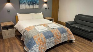 Een slaapkamer met een bed, twee nachtkastjes, een nachtkastje, een zwarte leren bank, een houten deur en een schilderij aan de muur.