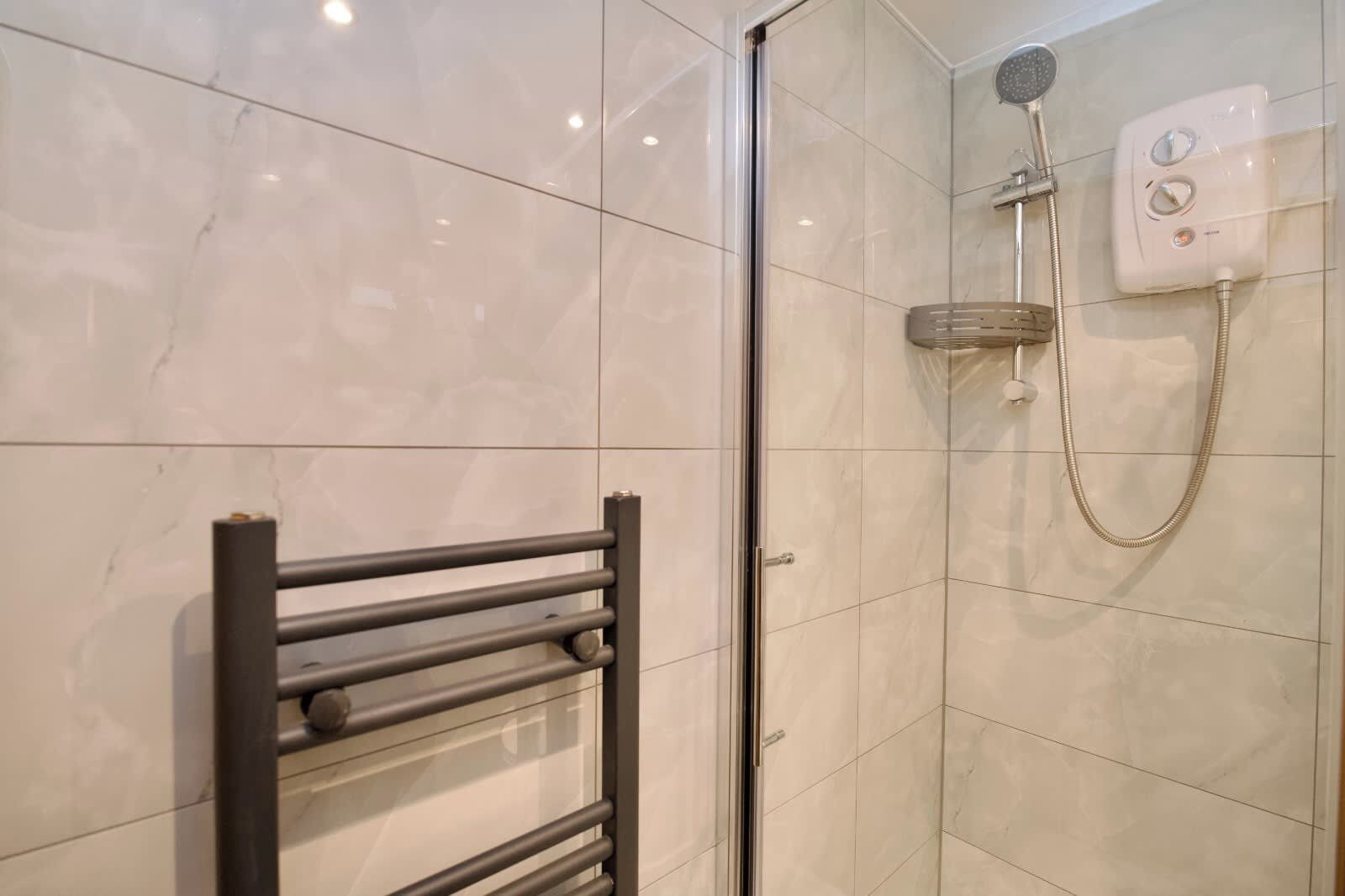 A modern bathroom with a glass shower enclosure, a handheld showerhead, and a control panel.
