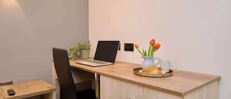 Ein zeitgemäßer Arbeitsplatz mit einem Laptop, einer Topfpflanze, einer Vase mit Blumen und einem Croissant auf einer Ablagefläche.