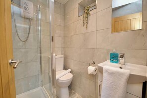 A modern bathroom with a glass-enclosed shower, a toilet, a sink with a towel, and a mirror. - Modern One Bedroom Apartment Near CBS Arena (West Midlands)