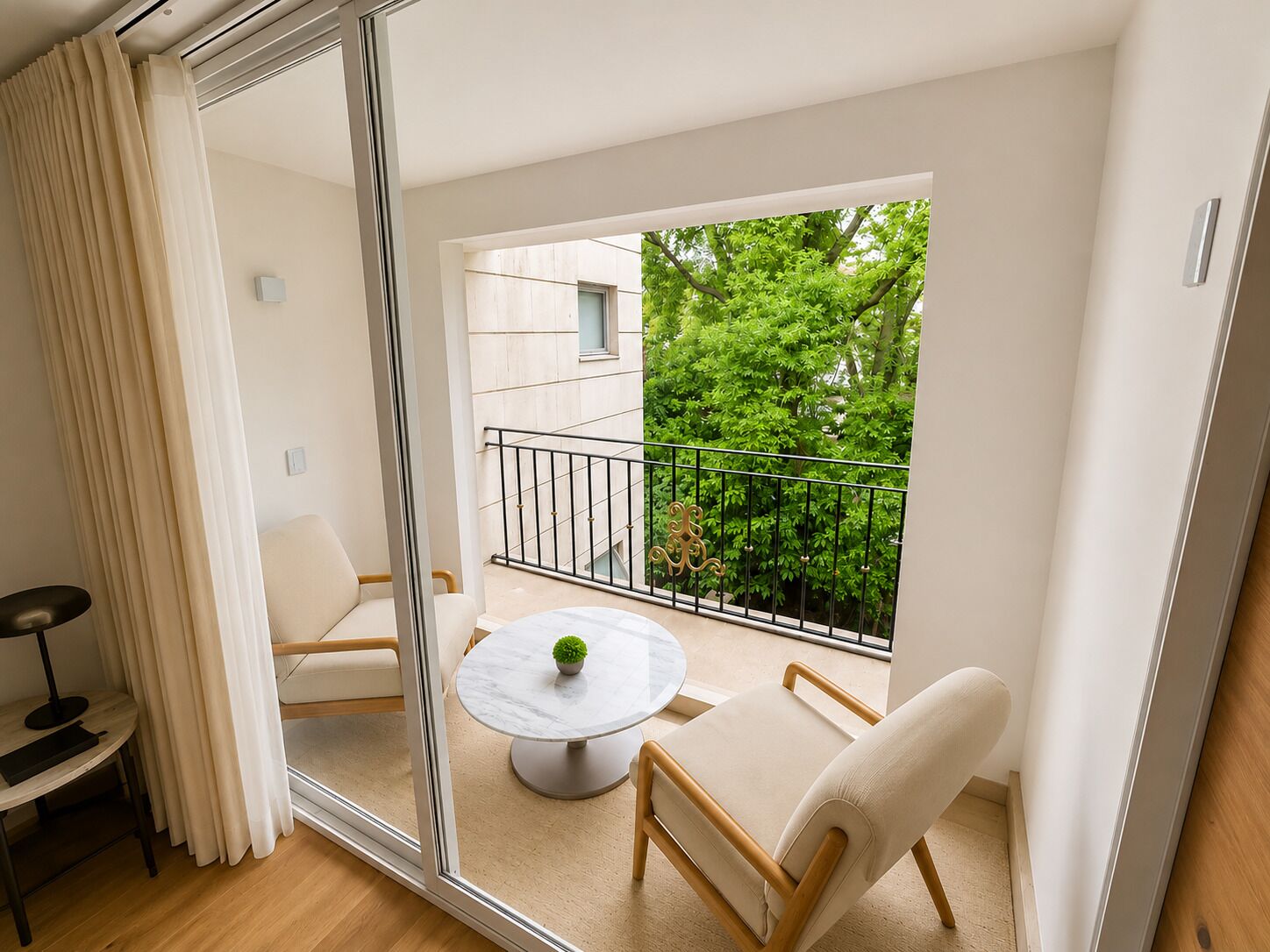Una sala de estar moderna con un separador de vidrio, una mesa redonda con una planta en maceta y vistas a un balcón con barandilla y vegetación.