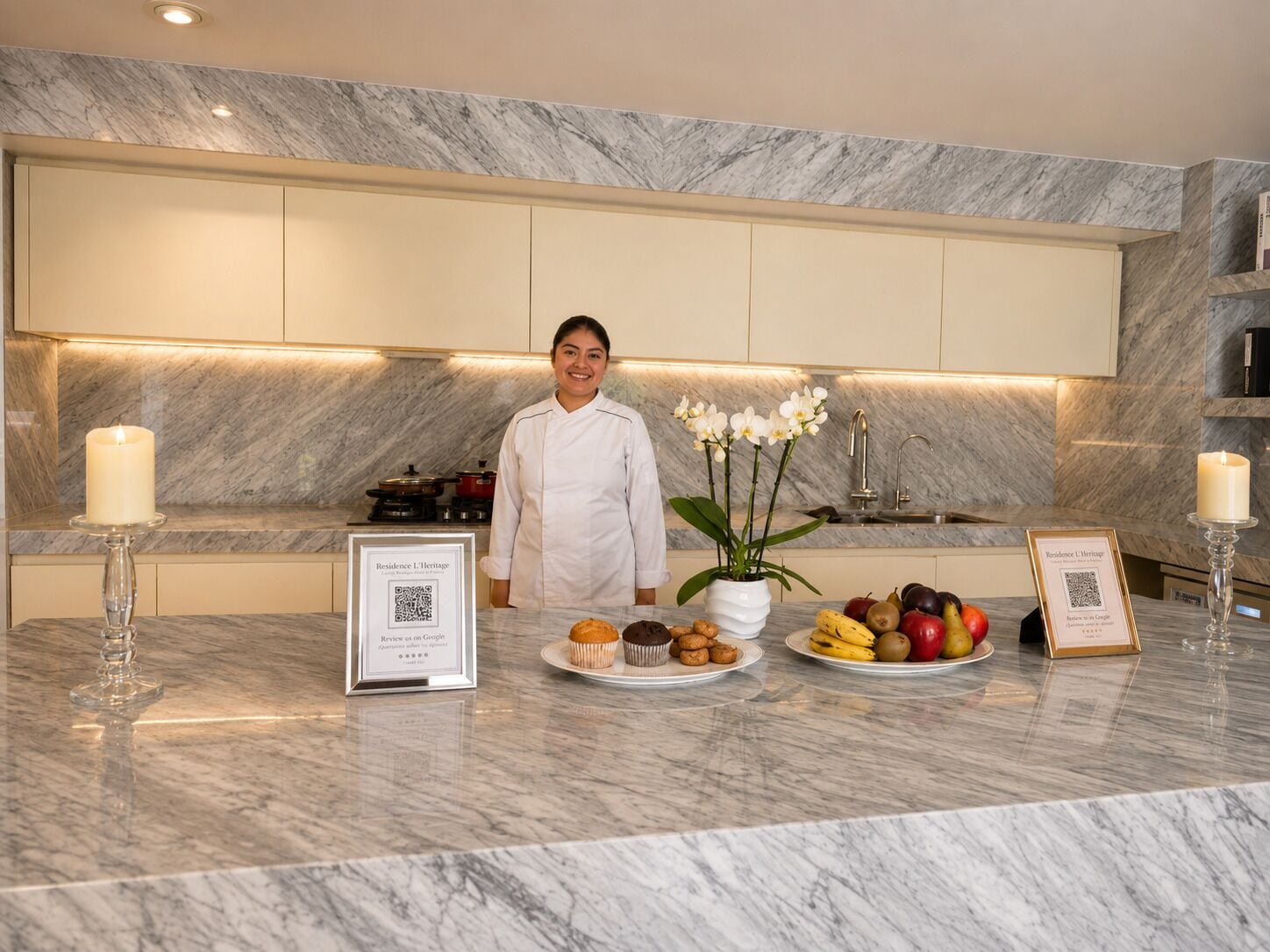 Una cocina moderna con encimeras de mármol, un chef de pie y una presentación de fruta y muffins.