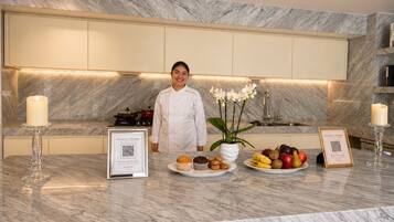 Una cocina moderna con encimeras de mármol, un chef de pie y una presentación de fruta y muffins.