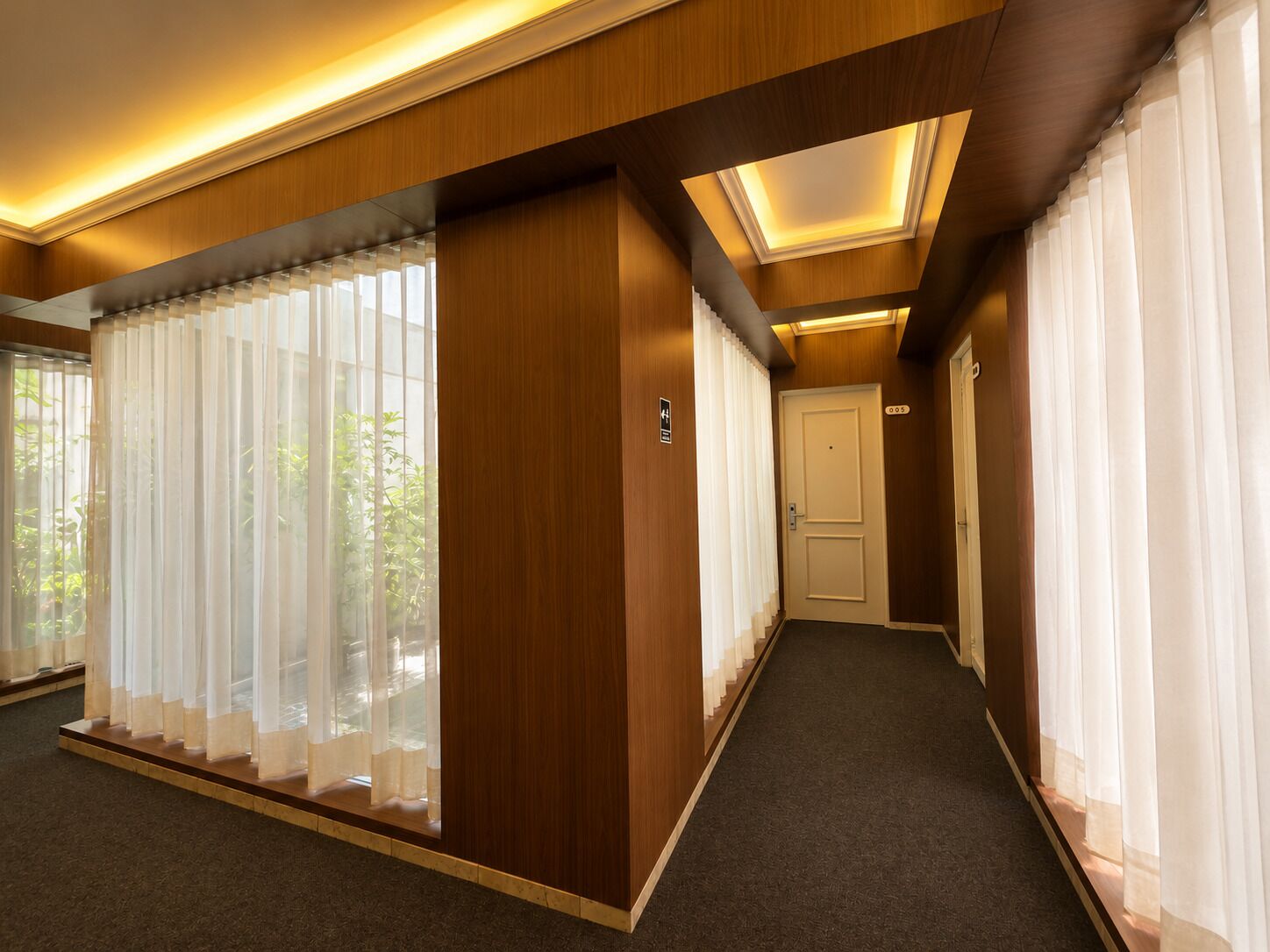 Un pasillo de hotel con piso alfombrado, paneles de madera y una puerta al final.