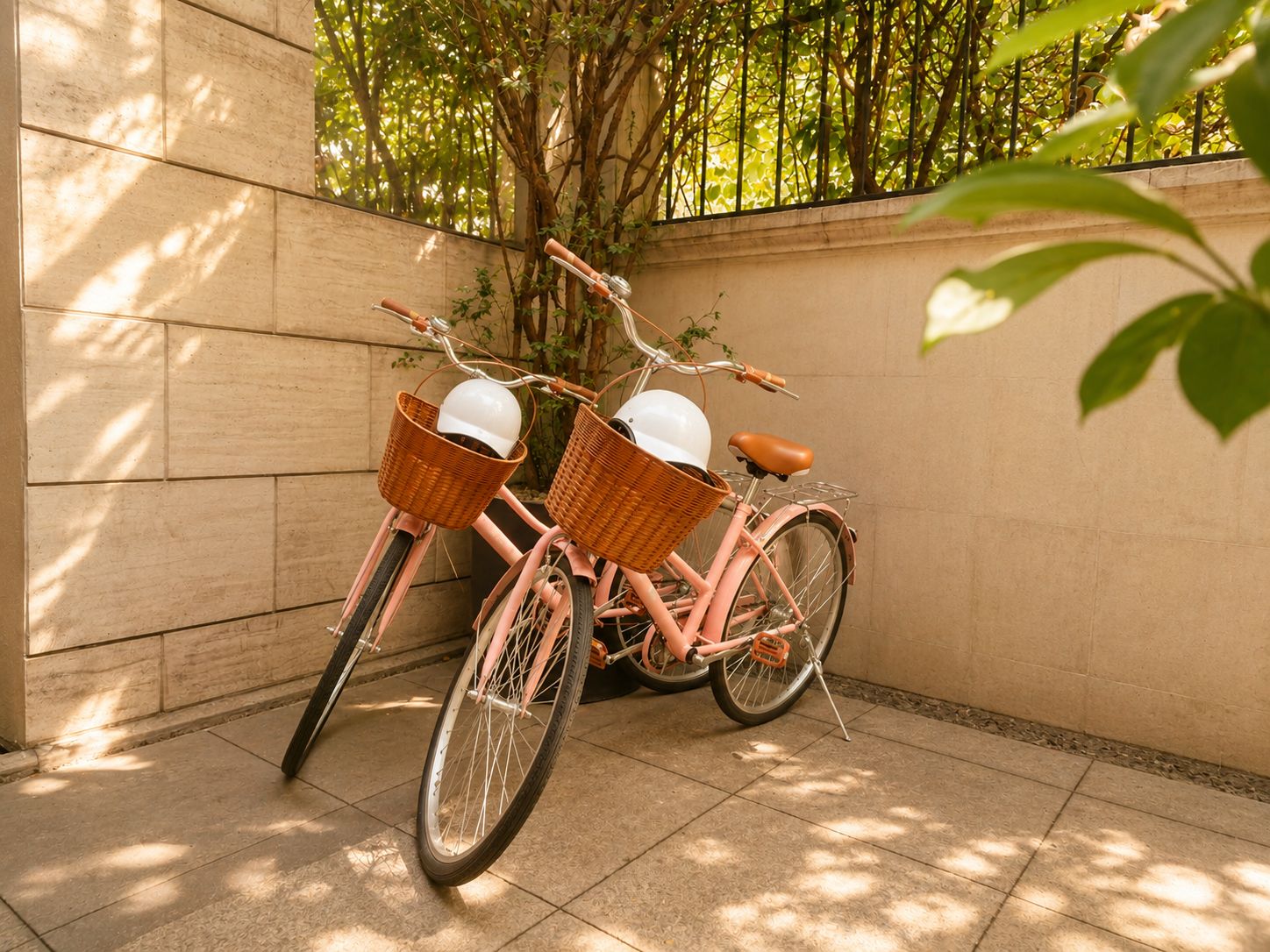 Un vélo rose avec deux paniers en osier, garé contre un mur, avec un arbre et une clôture en arrière-plan.