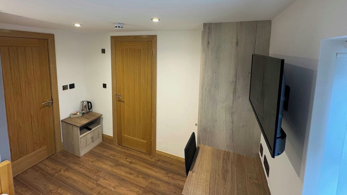 Une pièce de taille modeste, dotée d’un plancher en bois, d’un téléviseur fixé au mur et d’un petit coin cuisine.