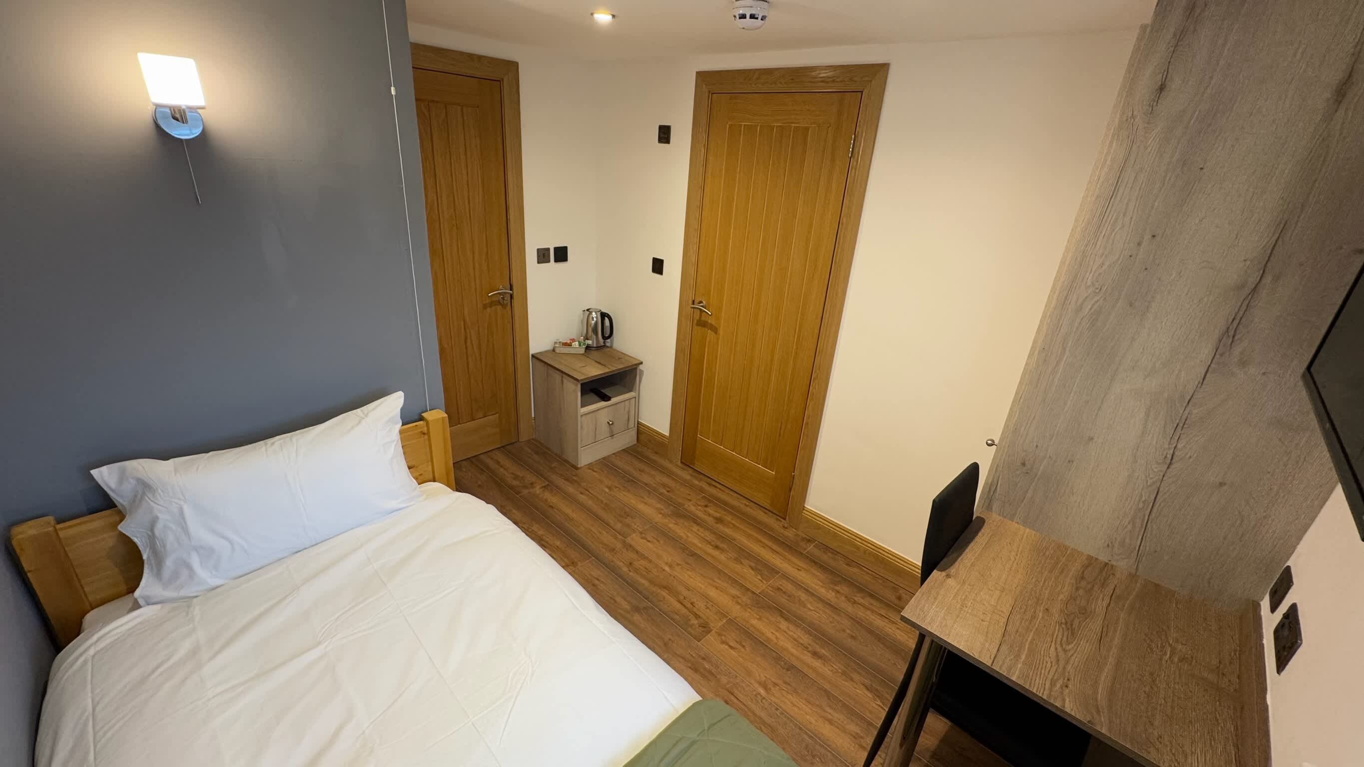 A hotel room with a bed, a bedside table, a small cabinet, a wooden wardrobe, and a television.