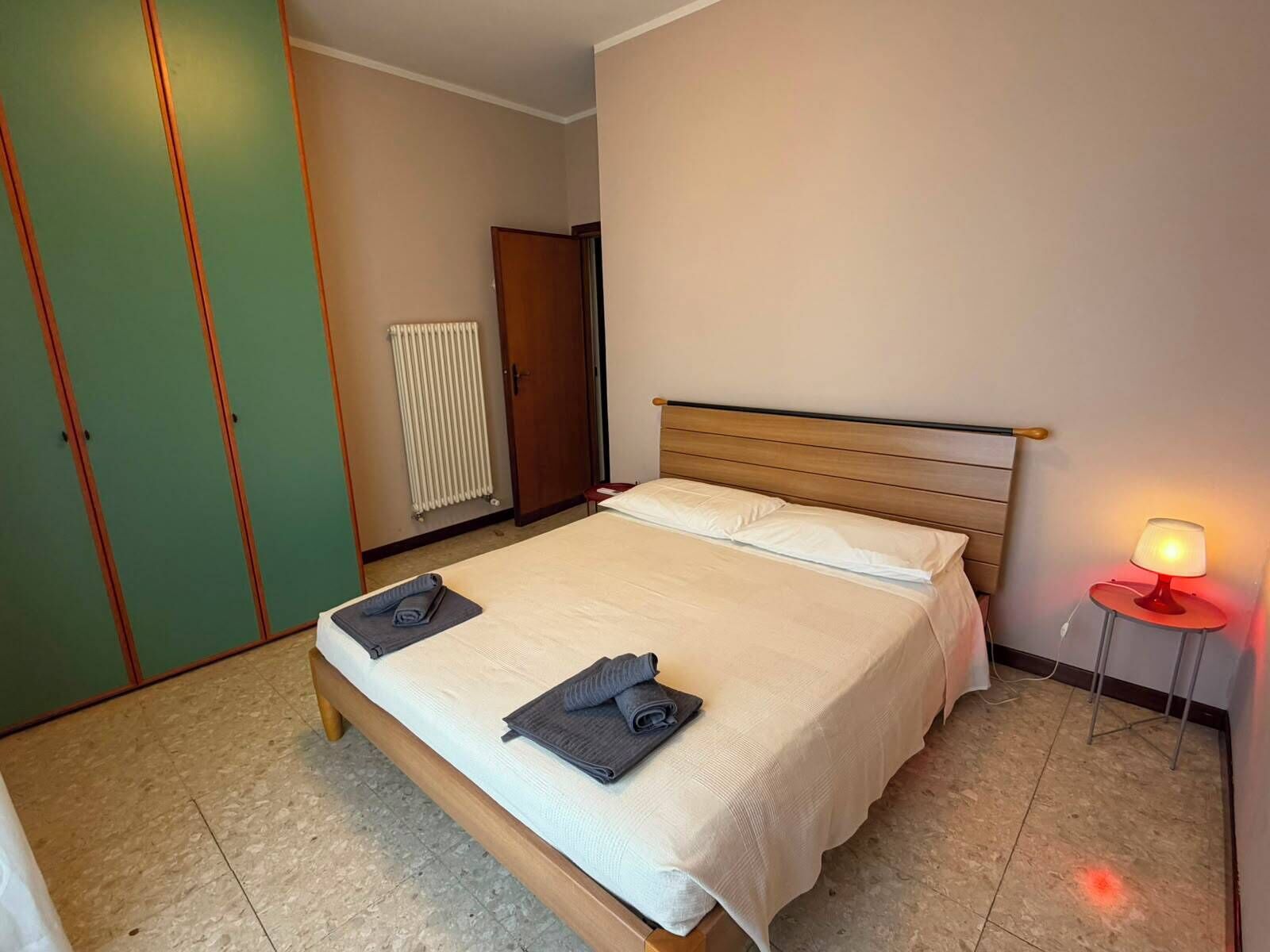 Un dormitorio con cama, radiador, armario y lámpara de noche.