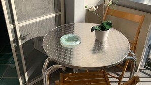 A round metal table with a glass top, accompanied by a wooden chair, positioned on a balcony with a view of a building. - Vrbo Property (Fondi)