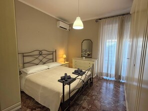 A bedroom with a bed, bedside lamp, dresser, mirror, and an air conditioning unit.