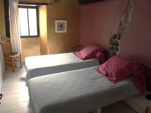 A room with two beds, a chair, a window with curtains, and a wall with a decorative element. - Holiday Home 'Gîte La Cerisaie' with Mountain Views, Shared Pool, and Wi-Fi (Saint-Prix)