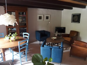 Un saló amb taula de dinar de fusta, cadires blaves, un sofà blau, una butaca de cuir marró, una televisió i una biblioteca.