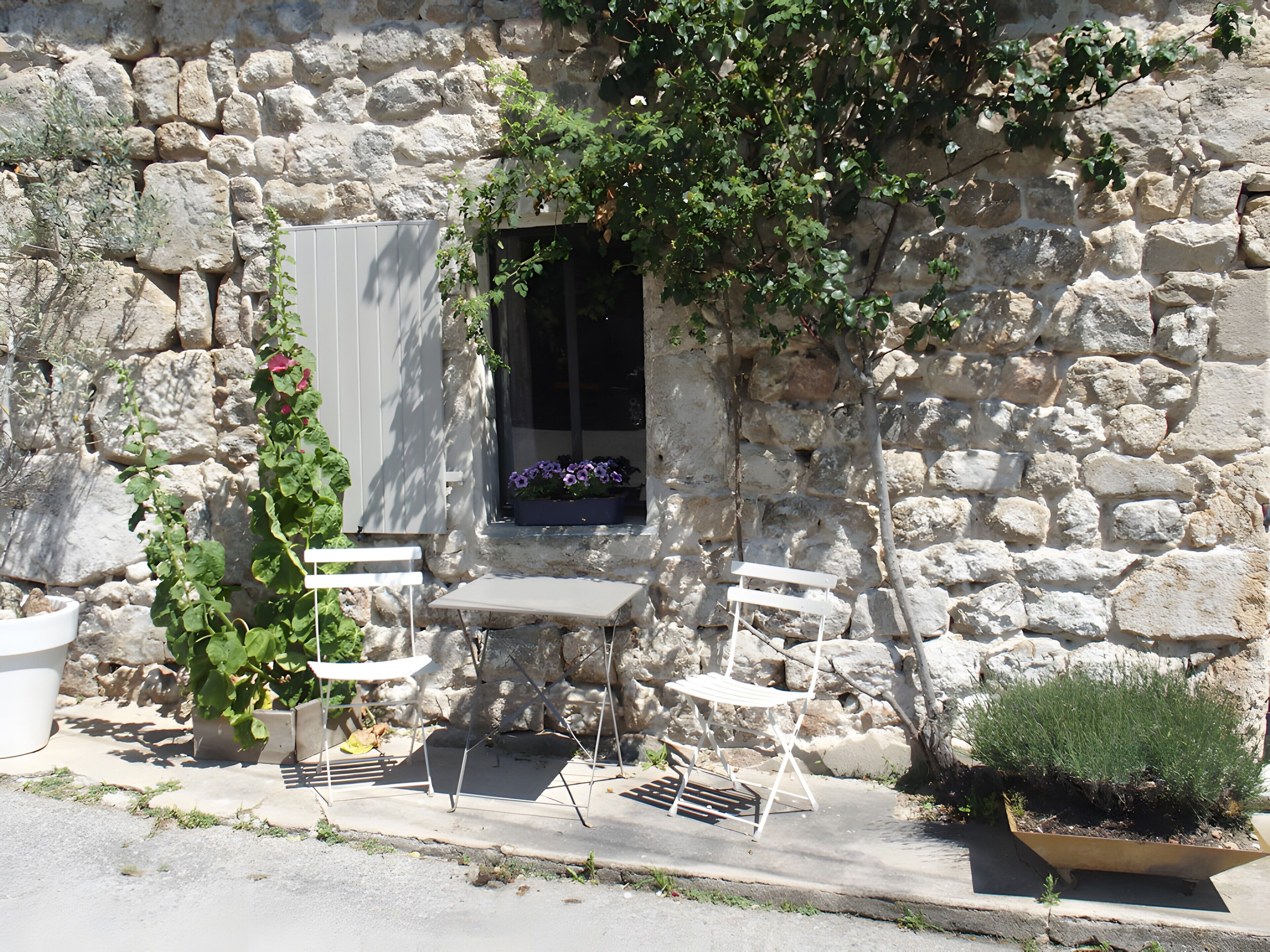Un bâtiment en pierre avec une fenêtre, un banc blanc et des plantes en pot.