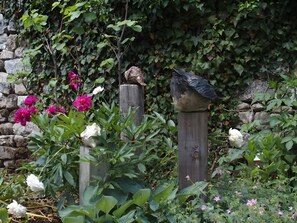 A garden with a wooden post, a birdhouse, and various plants including flowers. - Holiday Home 'Gîte La Cerisaie' with Mountain Views, Shared Pool, and Wi-Fi (Saint-Prix)