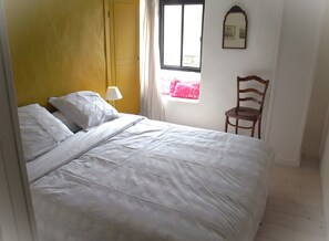 A bed with white bedding, a chair, a window with curtains, and a wall-mounted mirror. - Holiday Home 'Gîte La Cerisaie' with Mountain Views, Shared Pool, and Wi-Fi (Saint-Prix)
