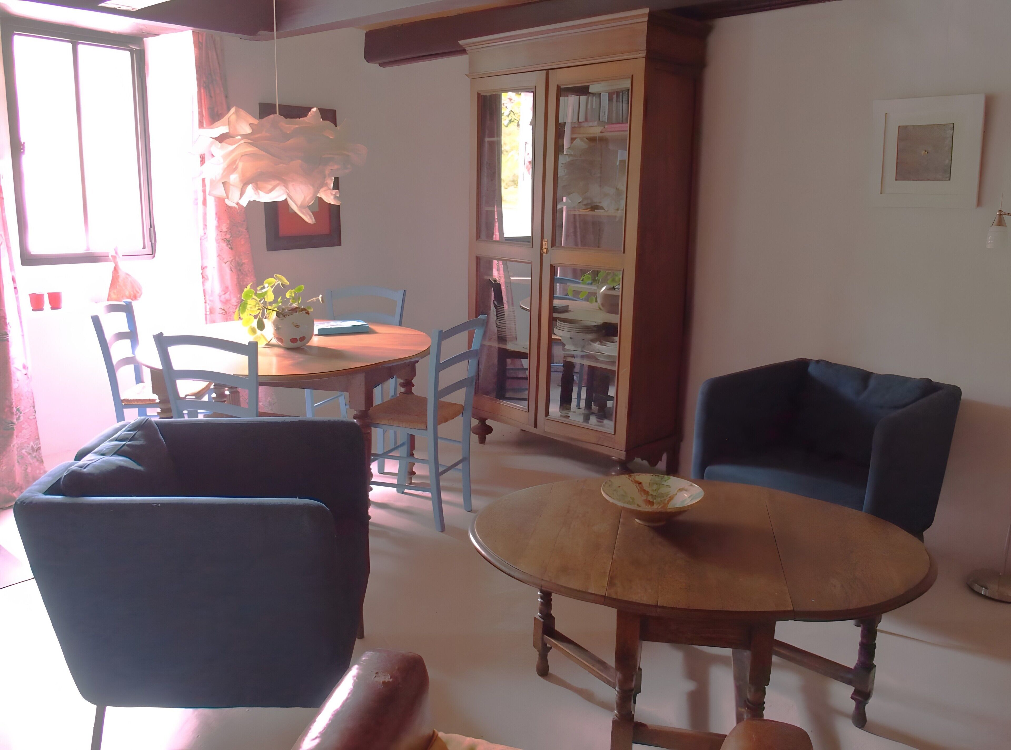 Un coin repas avec une table ronde en bois, un fauteuil bleu et un meuble avec des portes en verre.