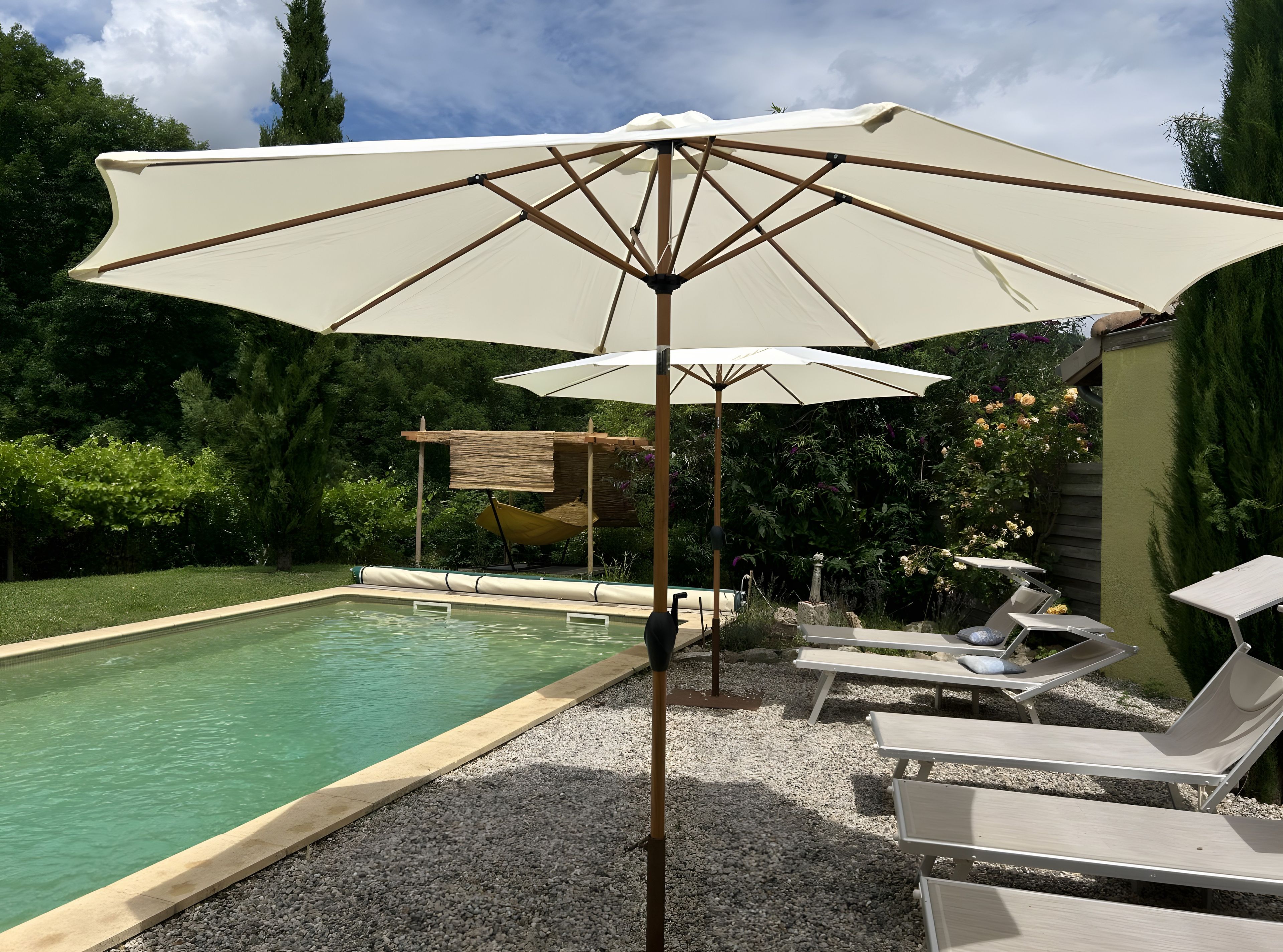 Zwembad met ligbedden en parasols, omringd door groen.