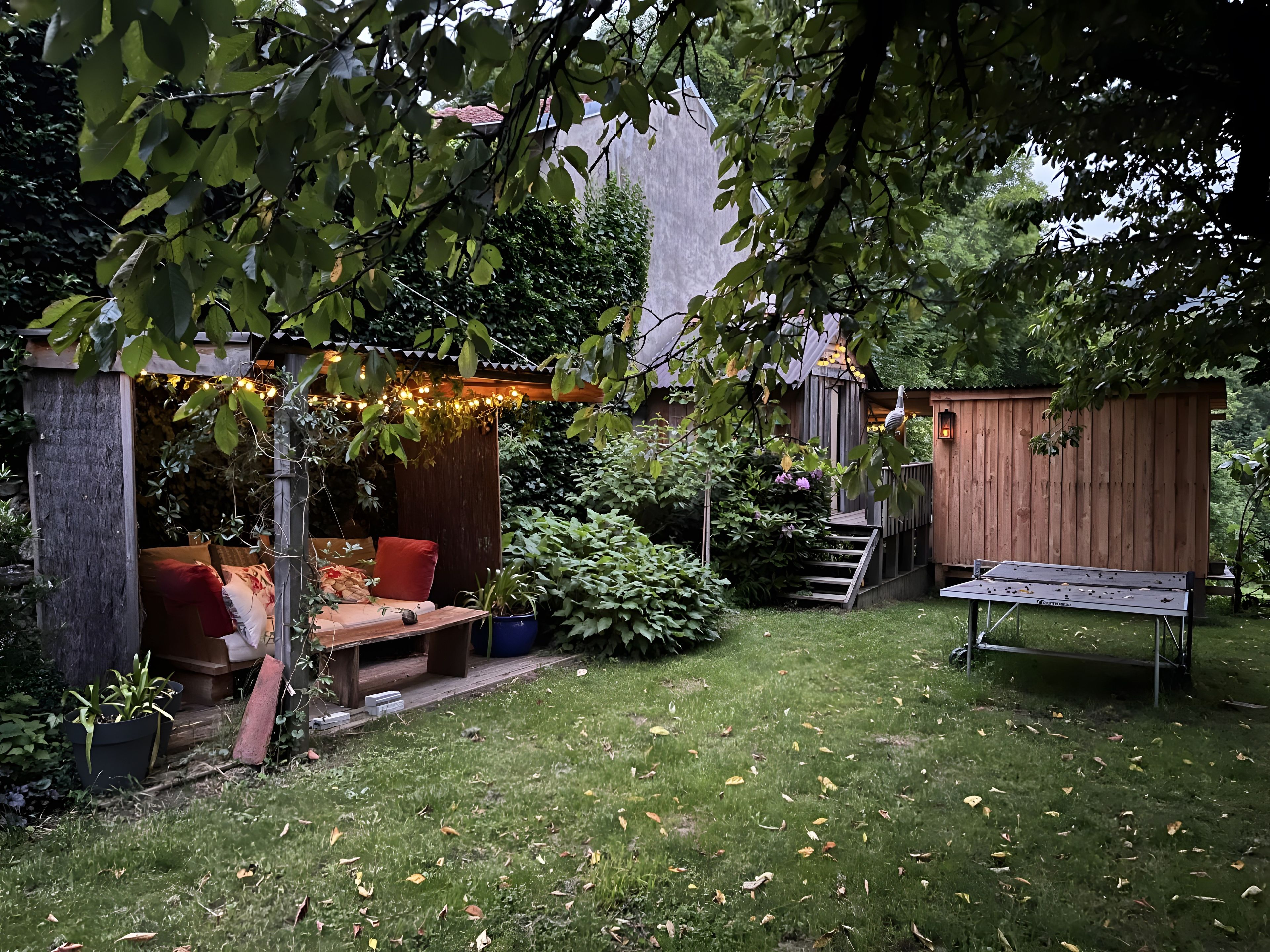 Ein Garten mit einer Holzterrasse, einer Bank und einem Pergola mit Lichterketten.