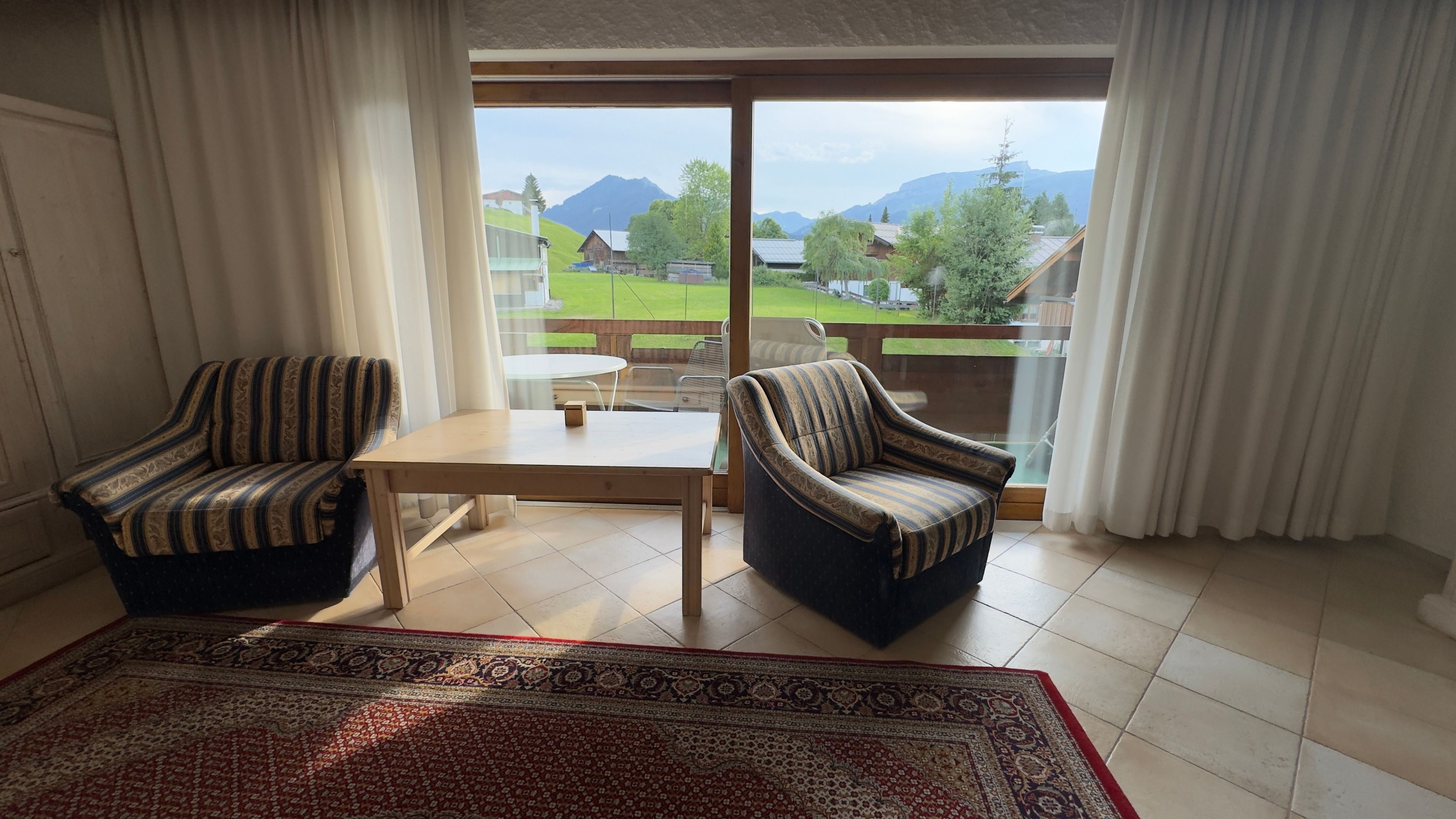 A room with two striped armchairs, a small table, and a view of a green landscape with mountains.