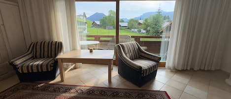 A room with two striped armchairs, a small table, and a view of a green landscape with mountains.