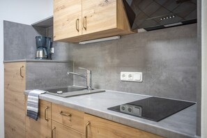 A modern kitchen with wooden cabinets, a stainless steel sink, a built-in stove, and a coffee maker. - Apartment '104 Arnika' with Mountain View, Balcony and Wi-Fi (Riezlern)