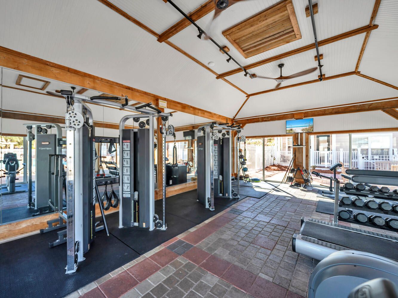 A gym with various exercise equipment, a wooden ceiling, and a view of the outside.