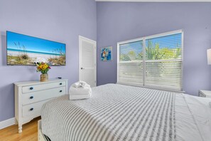Un dormitorio con cama, cómoda, un cuadro de una playa y una ventana con persianas.