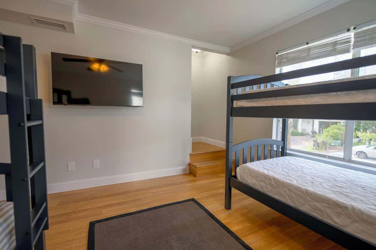 A room with a bunk bed, a television mounted on the wall, and a window with a view of the outside.