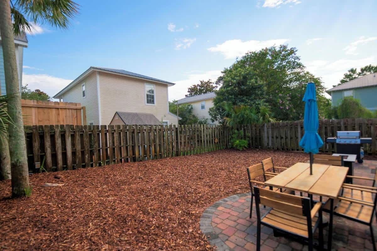 A backyard with a wooden deck, a barbecue grill, and a table with chairs.