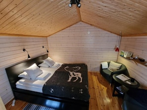 Een knus vertrek met een bed, een kleine zithoek en een houten plafond.