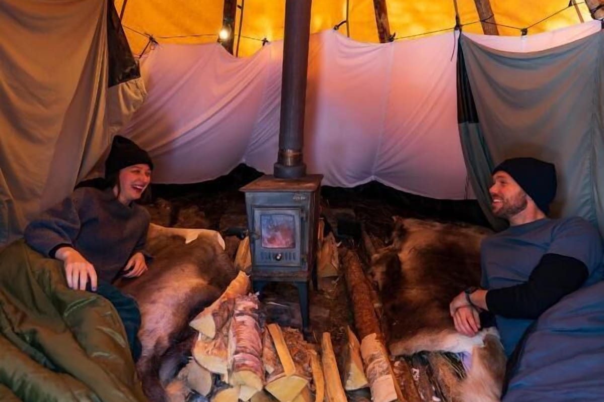 Een tent met een houtkachel, slaapzakken en een hond.