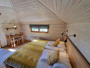 Een knus slaapkamer met een bed, kussens, een nachtkastje, een stoel, een raam en een hanglamp.