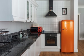 Uma cozinha com armários brancos, forno preto, torradeira vermelha e geladeira laranja.