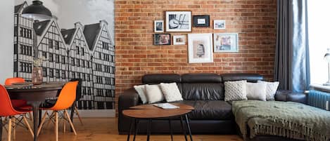 A living room with a brick wall, a sofa, a coffee table, and a dining area with chairs.