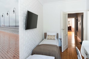 Ein Hotelzimmer mit weißer Backsteinwand, einem flachbildfernseher über dem Bett, Holzboden und Meerblick durch ein Fenster.