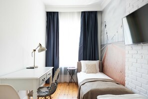 Quarto com cama, escrivaninha, cadeira, televisão e janela com cortinas.