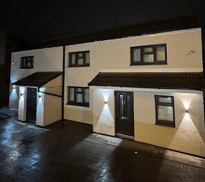 A two-story building with multiple windows and doors, illuminated by exterior lighting. - Modern Double Studio | Near CBS Arena (Kitchenette) (West Midlands)